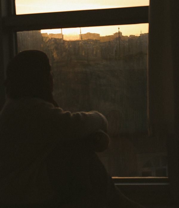 Person meditating peacefully near a window with a view of the evening city.